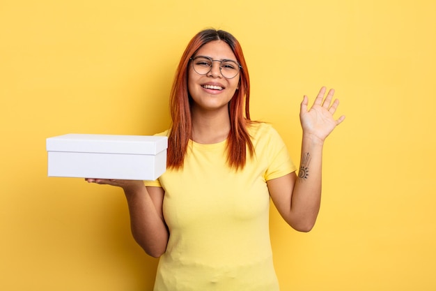 Mulher hispânica sorrindo alegremente acenando com a mão dando as boas-vindas e cumprimentando você conceito de embalagem vazia