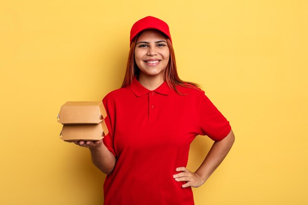 Mulher hispânica sorrindo alegremente com uma mão no quadril e confiante. take away entregar conceito