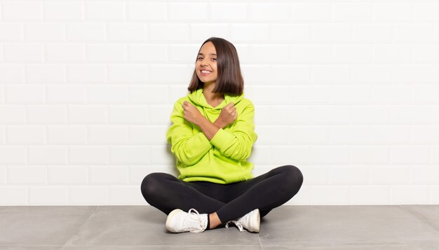 Mulher hispânica sorrindo alegremente e comemorando, com os punhos cerrados e os braços cruzados, sentindo-se feliz e positiva