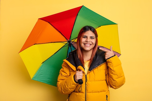 Mulher hispânica sorrindo com confiança apontando para próprio sorriso largo. conceito de chuva e guarda-chuva