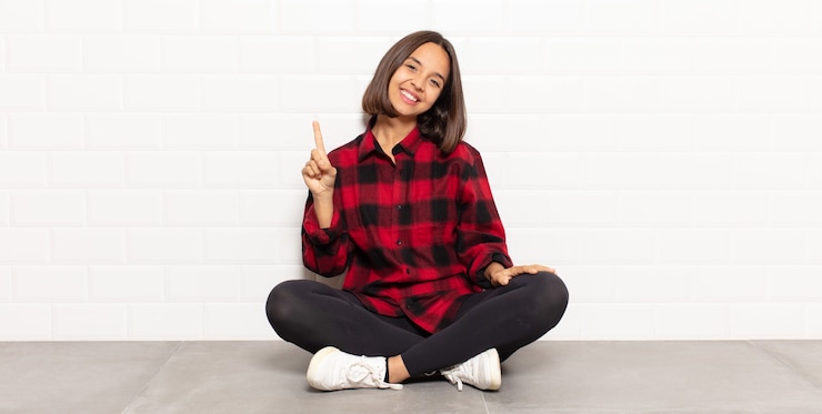 Foto mulher hispânica sorrindo e parecendo amigável, mostrando o número um ou primeiro com a mão para a frente, em contagem regressiva