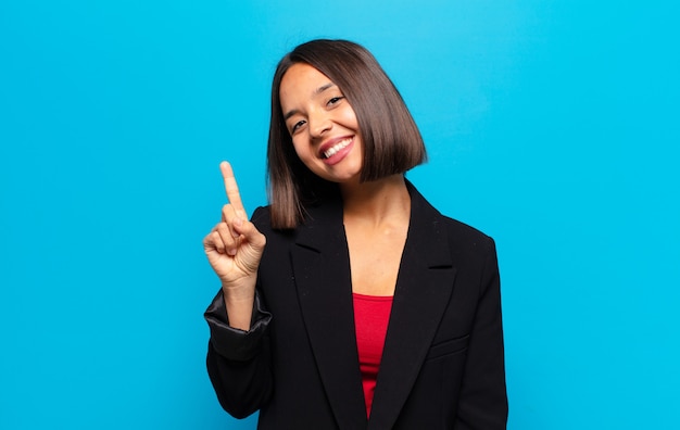 Mulher hispânica sorrindo e parecendo amigável, mostrando o número um ou primeiro com a mão para a frente, em contagem regressiva