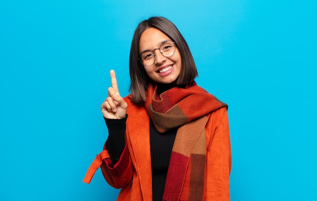 Mulher hispânica sorrindo e parecendo amigável, mostrando o número um ou primeiro com a mão para a frente, em contagem regressiva