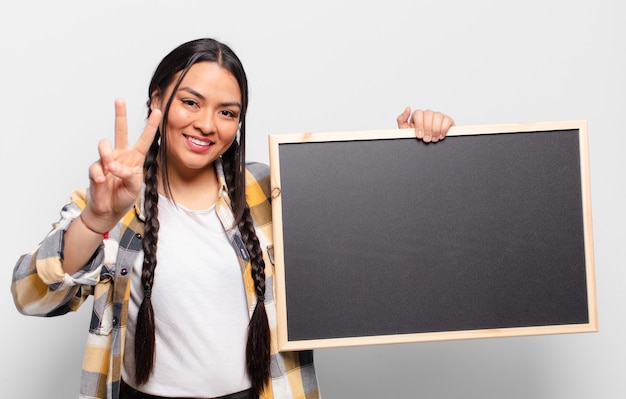 Mulher hispânica sorrindo e parecendo feliz, despreocupada e positiva, gesticulando vitória ou paz com uma mão