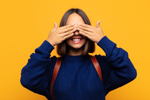 Mulher hispânica sorrindo e se sentindo feliz, cobrindo os olhos com as duas mãos e esperando por uma surpresa incrível