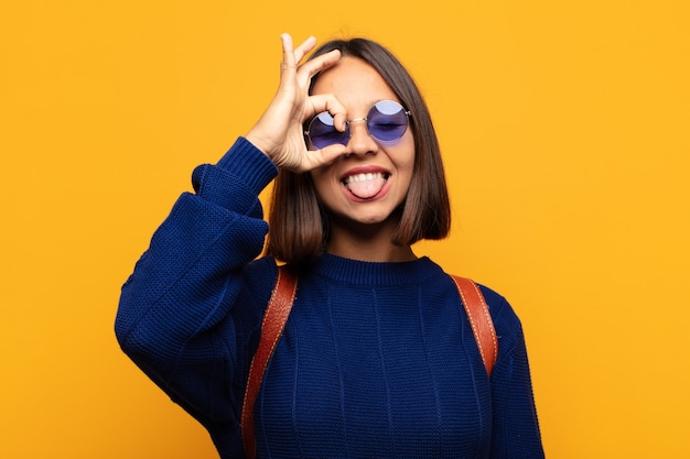 Mulher hispânica sorrindo feliz com careta engraçada, brincando e olhando pelo olho mágico, espionando segredos