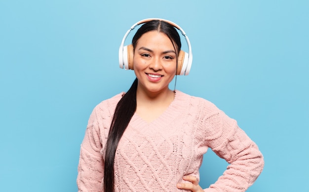 Mulher hispânica sorrindo feliz com uma mão no quadril e uma atitude confiante, positiva, orgulhosa e amigável