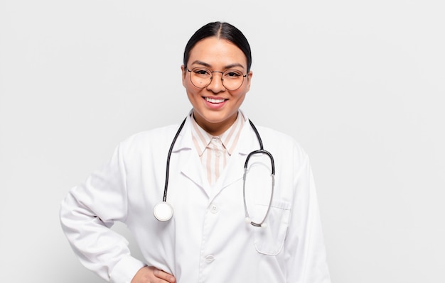 Mulher hispânica sorrindo feliz com uma mão no quadril e uma atitude confiante, positiva, orgulhosa e amigável