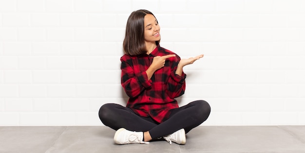 Mulher hispânica sorrindo, sentindo-se feliz, despreocupada e satisfeita, apontando para um conceito ou ideia no espaço da cópia ao lado