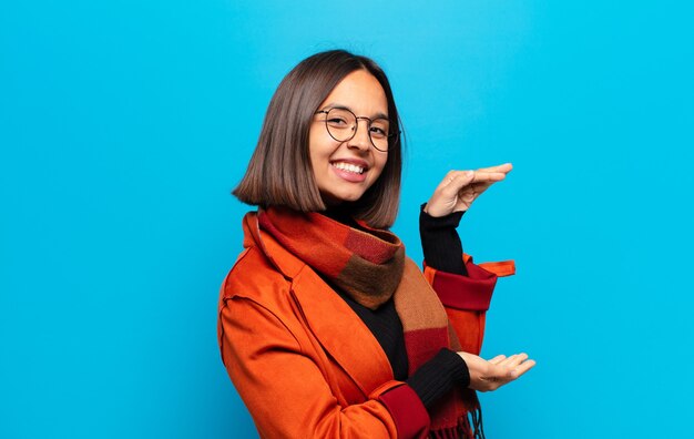 Mulher hispânica sorrindo, sentindo-se feliz, positiva e satisfeita, segurando ou mostrando um objeto ou conceito no espaço da cópia