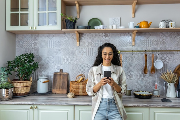 Mulher hispânica usa celular em casa na cozinha mulher sorri e se alegra lê mensagens