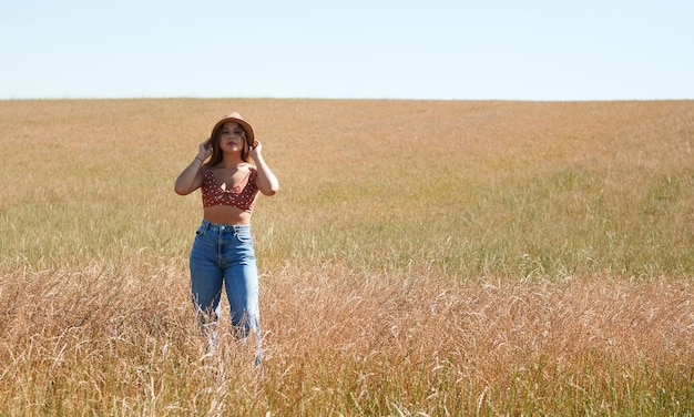 Mulher hispânica usando um chapéu posando em um campo de trigo em um dia ensolarado