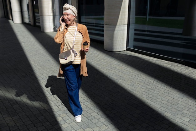 Mulher idosa ao ar livre na cidade falando ao telefone enquanto toma café