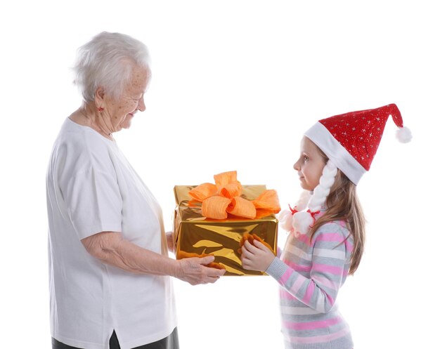 Mulher idosa apresentando uma caixa de presente para a neta com chapéu de Papai Noel no estúdio sobre fundo branco