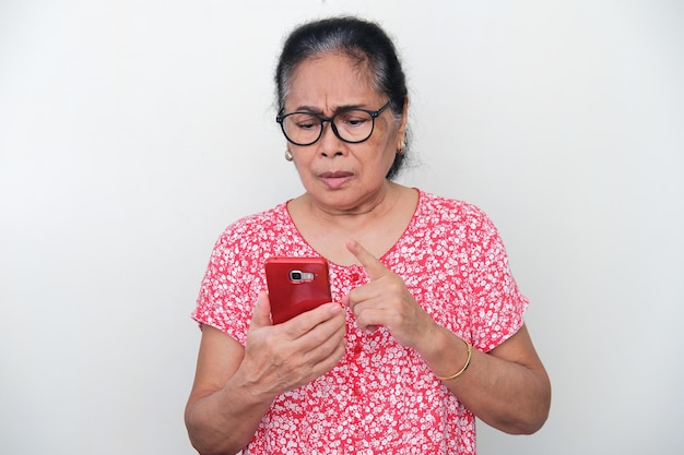 Mulher idosa asiática apontando o dedo para o celular com expressão de tristeza