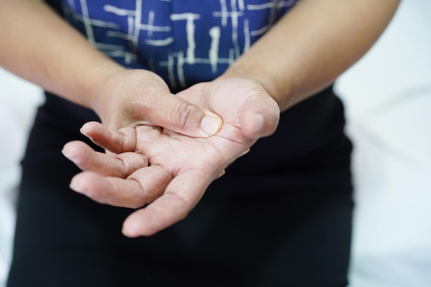 Mulher idosa asiática dói sua mão e dedo a tenossinovite de De Quervain