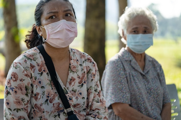 Mulher idosa asiática e filha no banco sentado de distanciamento social e usando máscara facial para proteger a infecção de segurança covid 19 coronavirus no parque