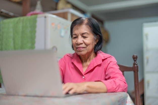 Mulher idosa asiática feliz aprendendo a usar um laptop em casa