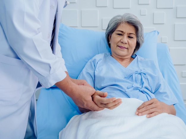 Mulher idosa asiática feliz sorrindo na cama enquanto médico de jaleco branco segurando a mão para verificação para examinar o pulso cardíaco na sala de recuperação no hospital Conceito de verificação de saúde médica