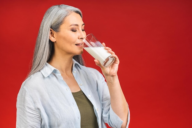 Mulher idosa asiática idosa bebendo leite para alimentos de cálcio e conceito de estilo de vida saudável isolado em fundo vermelho