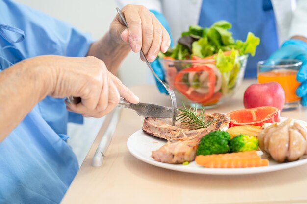 Mulher idosa asiática idosa paciente tomando café da manhã e comida vegetal saudável com esperança e feliz enquanto está sentada e com fome na cama no hospital