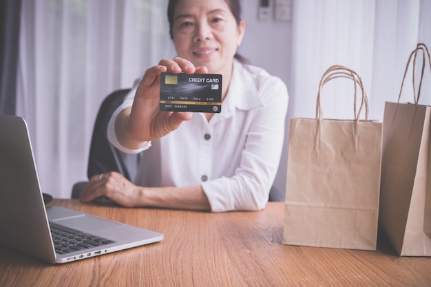 Mulher idosa asiática que mostra a zombaria acima do cartão de crédito, conceito de comprar em linha.