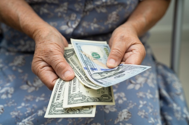 Mulher idosa asiática segurando e contando dinheiro de notas de dólar americano na bolsa Problema de economia de pobreza na aposentadoria