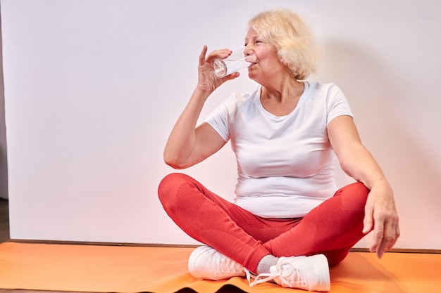 Mulher idosa bebendo água doce após exercícios esportivos no chão, descanse. conceito de estilo de vida saudável