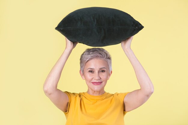 Mulher idosa bonita e elegante com um travesseiro nas mãos sobre um fundo amarelo