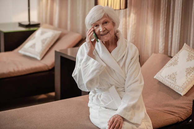 Mulher idosa bonita em roupão branco com um telefone nas mãos