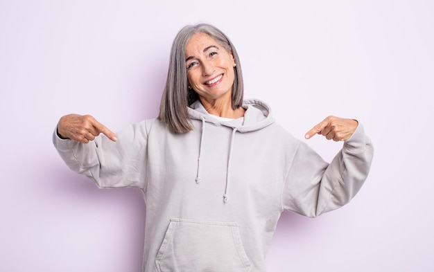 Mulher idosa bonita parecendo orgulhosa, arrogante, feliz, surpresa e satisfeita, apontando para si mesma, sentindo-se uma vencedora