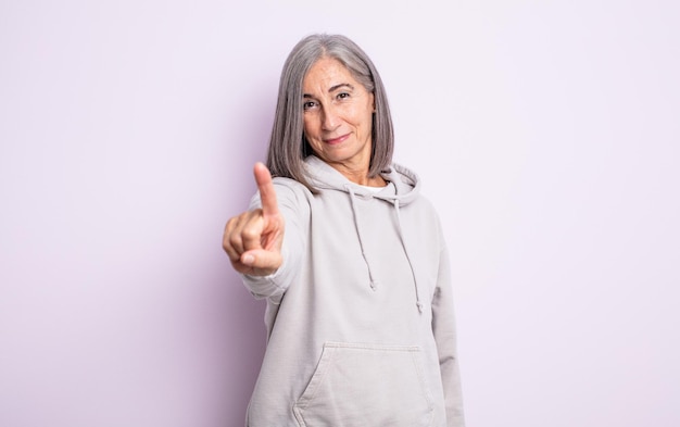 Mulher idosa bonita sorrindo com orgulho e confiança fazendo a pose número um triunfantemente, sentindo-se uma líder