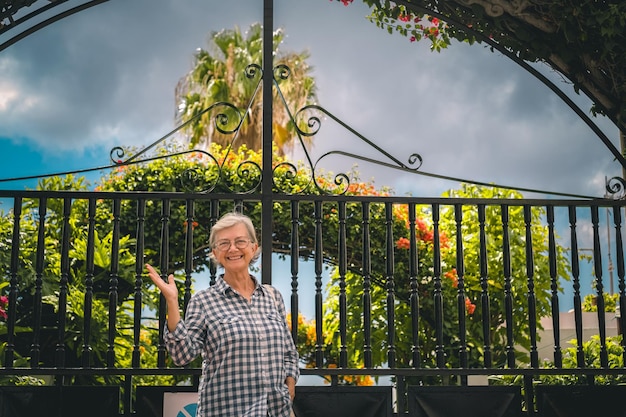 Mulher idosa caucasiana sorridente caminhando ao ar livre em um jardim florido olhando para a câmera Estilo de vida de aposentadoria relaxado