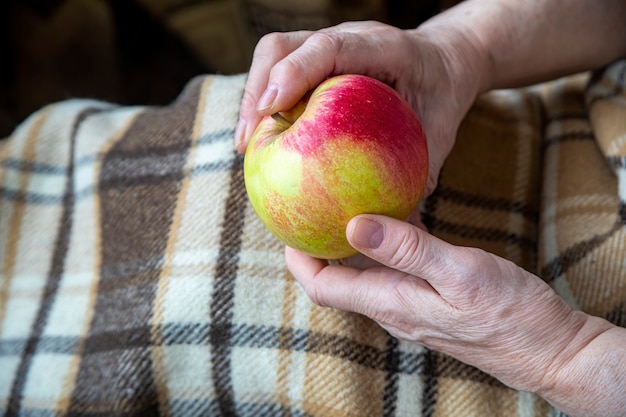 Mulher idosa com as mãos segurando uma maçã como um presente para uma próxima geração.