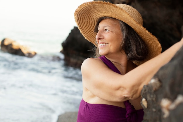 Foto mulher idosa com chapéu de palha aproveitando o dia na praia