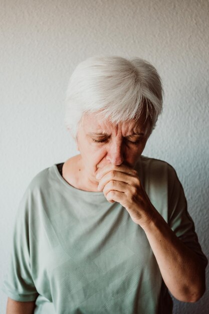 Foto mulher idosa com gripe de pé contra a parede