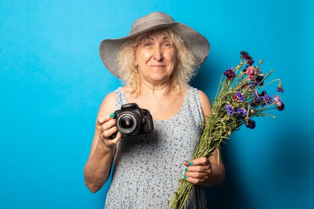 Mulher idosa com um chapéu de aba larga e vestido segurando um buquê de flores