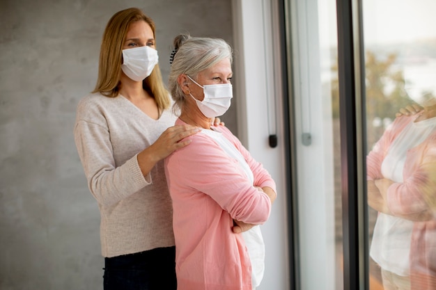 Mulher idosa com uma filha carinhosa em casa usando máscaras médicas como proteção contra o coronavírus