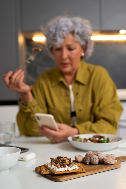 Foto mulher idosa comendo prato de figos em casa e usando smartphone