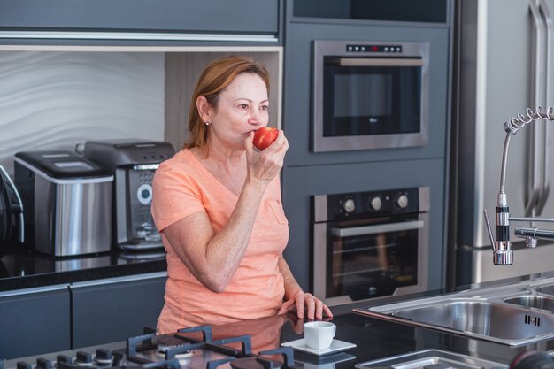 Mulher idosa comendo uma maçã na cozinha