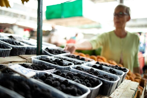 mulher idosa comprando amoras frescas no mercado e segurando uma sacola cheia de alimentos saudáveis