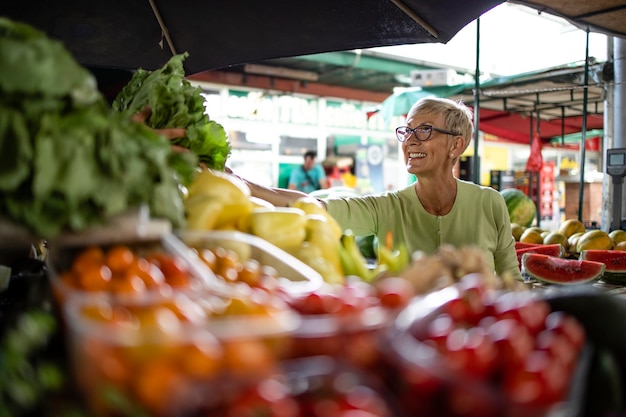 Mulher idosa comprando vegetais orgânicos frescos no mercado para uma alimentação saudável.