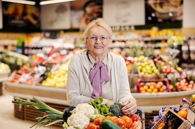 Mulher idosa comprando vegetais orgânicos no supermercado e sorrindo para a câmera