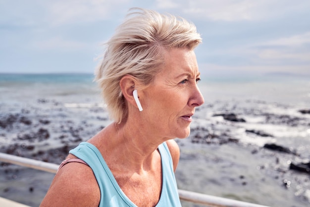 Mulher idosa correndo na praia com fones de ouvido para bem-estar energético ou treino saudável Exercício feminino idoso e fitness no oceano de esportes cardio maratona ou ouvindo música para mentalidade forte