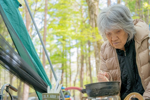 Mulher idosa cozinhando no acampamento