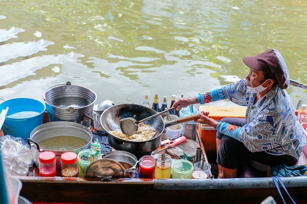 Mulher idosa cozinhando omelete no barco Wat Takhian Floating Market em Nonthaburi