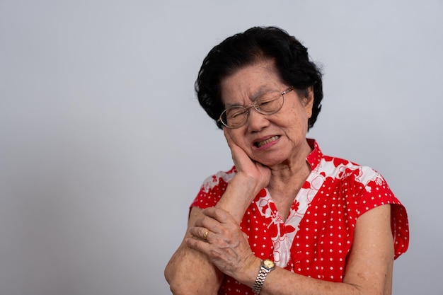 Mulher idosa da Ásia sofrendo de dor de dente severa segurando sua bochecha e sofrendo dentes fortes