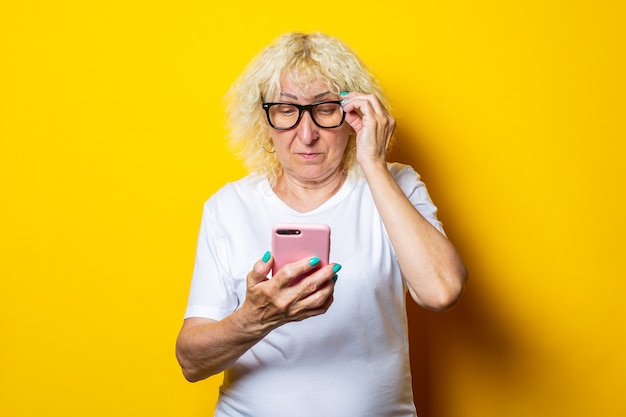 Mulher idosa de camiseta branca com óculos olhando para o telefone