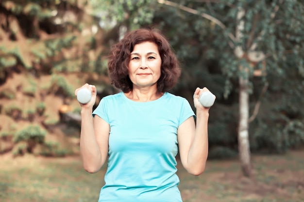 Mulher idosa de meia-idade ativa fazendo exercícios com halteres em um parque ao ar livre