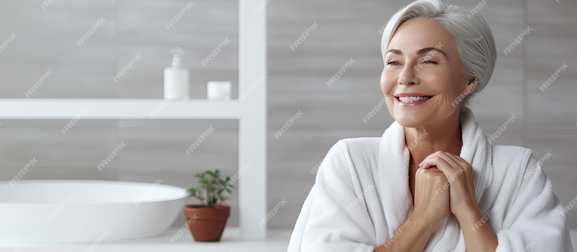 Mulher Bonita E Satisfeita Olhando Para O Espelho No Banheiro, Sentindo-se  Bonita E Atraente, Menina Feliz Usando Roupão Branco Tocando A Pele Lisa  Perfeita Do Rosto, Desfrutando Da Rotina De Cuidados Com